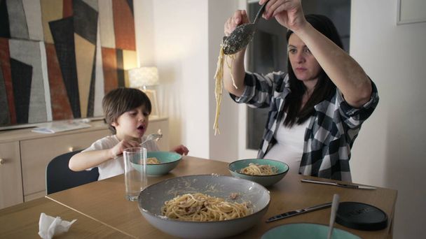 Вечеря разом - мати, що подає пасту спагетті на тарілці, поки син їсть їжу, гаряча їжа Бонд вдома - Фото, зображення
