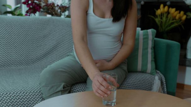 Femme enceinte buvant de l'eau sur le canapé prenant soin de la santé au troisième trimestre - Photo, image