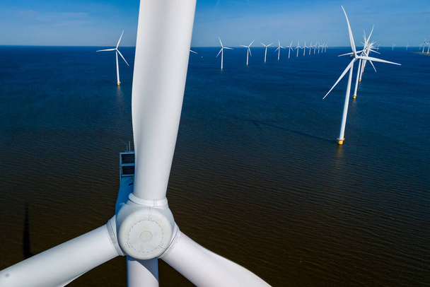 Промені сонячного світла освітлюють величезну вітрову електростанцію в океані, демонструючи ряд елегантних вітряних турбін, що стоять високо в Нідерландах Flevoland під час яскравого сезону весни. - Фото, зображення