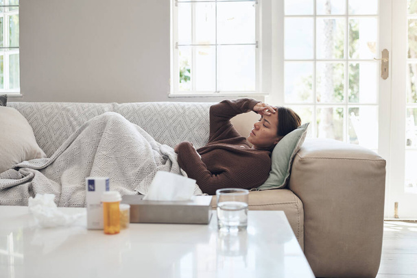 Mujer, enfermo y dolor de cabeza con medicamentos en el sofá para la gripe, el resfriado o los senos paranasales en la sala de estar en casa. Mujer cansada con enfermedad, fiebre o gripe en la fatiga o dormida en el sofá de paracetamol. - Foto, imagen
