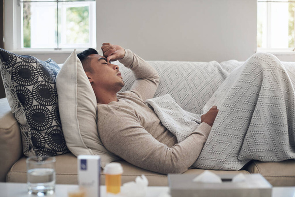 Homem doente, dor de cabeça e medicação com gripe, sinus ou dor de doença no sofá da sala de estar em casa. Cansado do sexo masculino com enxaqueca de febre alta, gripe ou infecção no sofá lounge em casa. - Foto, Imagem