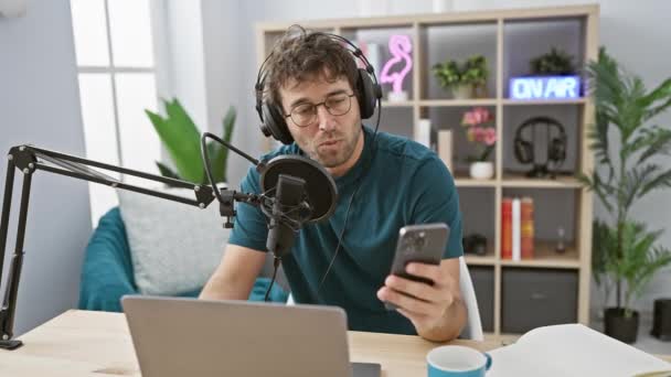 İspanyol bir adam modern bir stüdyoda mikrofon, dizüstü bilgisayar ve canlı yayın ile bir podcast sunuyor. - Video, Çekim