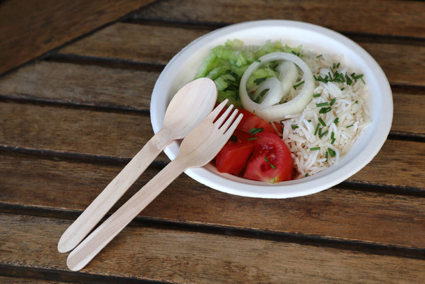 Detail of wooden disposable cutlery with food in chinet disposable bowl on wooden table - takeaway food concept, eco friendly, space for text - Photo, Image