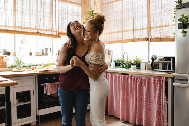 Joyful laughter fills the kitchen as two friends share a close and amusing moment in a homely atmosphere. - Photo, Image