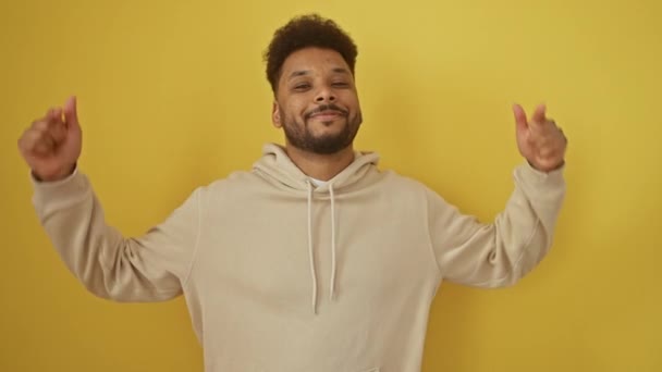 Handsome african american guy in hoodie, confidently pointing at self with great pride. happy expression caught in isolated yellow background portrait - Footage, Video