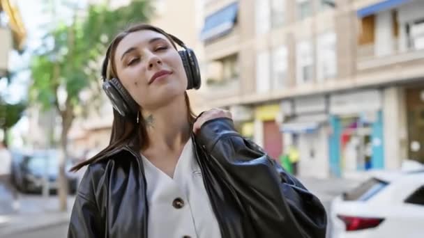 Młoda kobieta ciesząca się muzyką ze słuchawkami na ulicy miasta - Materiał filmowy, wideo