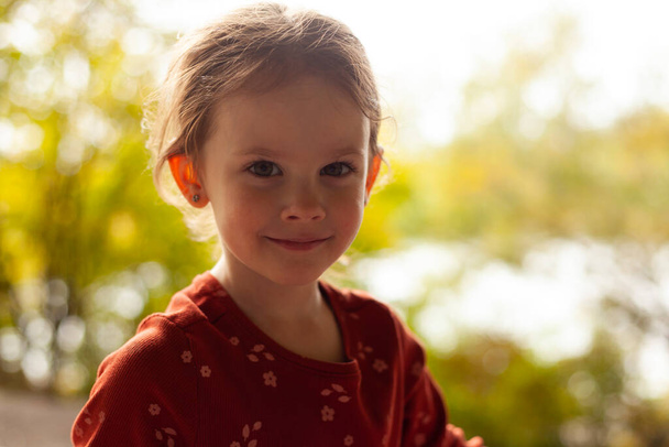 маленька красива дівчина в червоній сорочці на тлі розмитого листя - Фото, зображення