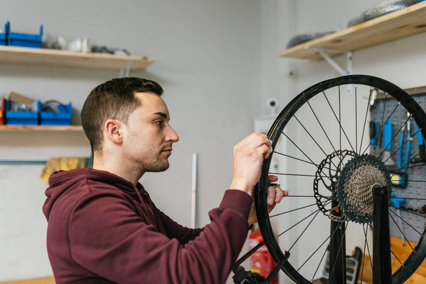 Механик велосипеда проверяет и ремонтирует задние колеса и спицы велосипеда в своей мастерской.. - Фото, изображение