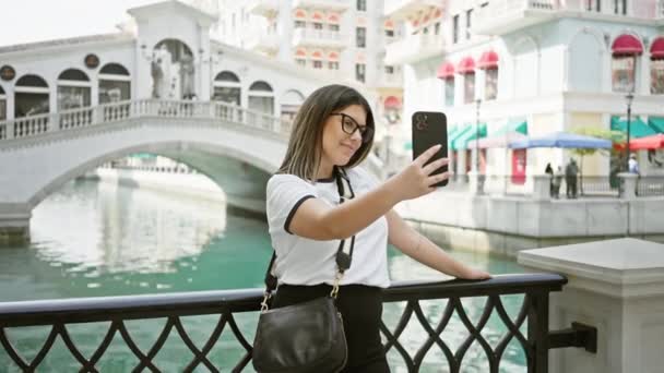 Mladá žena používá smartphone, aby se selfie v doha je qanat quartier s italsky inspirovaný architekturou v pozadí. - Záběry, video