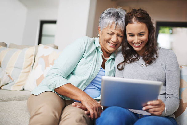 Help, tablet and woman teaching senior mother networking on internet, mobile app or website on sofa. Happy, bonding and elderly mom learning digital technology with female person in living room - Photo, Image
