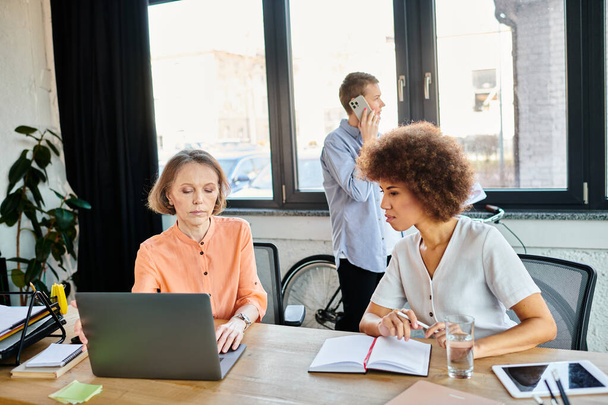 Profissionais trabalhadoras e diversas colaboram em torno de uma mesa com laptops em um ambiente de escritório moderno. - Foto, Imagem