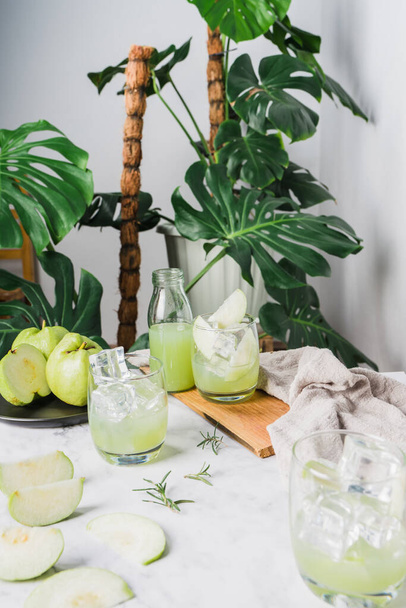 Osvěžující lahodný z ledové guava šťávy ve sklenici a nakrájené guava umístěn na bílém mramoru, houseplant zelené rostlinné pozadí. Dekorativní kompoziční nápoje doma. Svislá fotografie - Fotografie, Obrázek