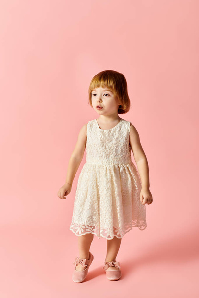 Słodka dziewczyna w białej sukience stoi wdzięcznie na tętniącym życiem różowym tle. - Zdjęcie, obraz