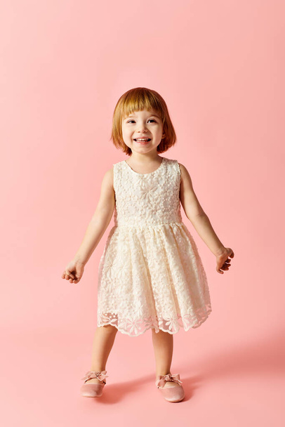 Little girl in white dress poses gracefully on pink backdrop. - Photo, Image