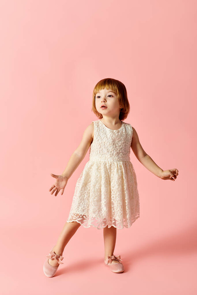 白いドレスの小さな女の子は鮮やかなピンクの背景にポーズを打つ. - 写真・画像