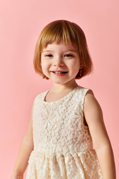 Κοριτσάκι με λευκό φόρεμα ποζάρει για ένα πορτραίτο σε ροζ φόντο. - Φωτογραφία, εικόνα