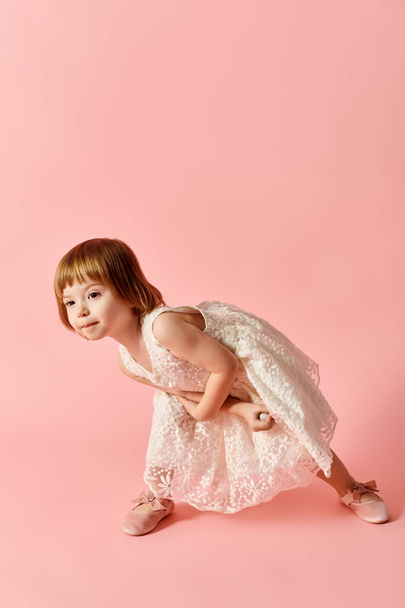 Une petite fille en robe blanche se dresse avec charme sur un fond rose. - Photo, image