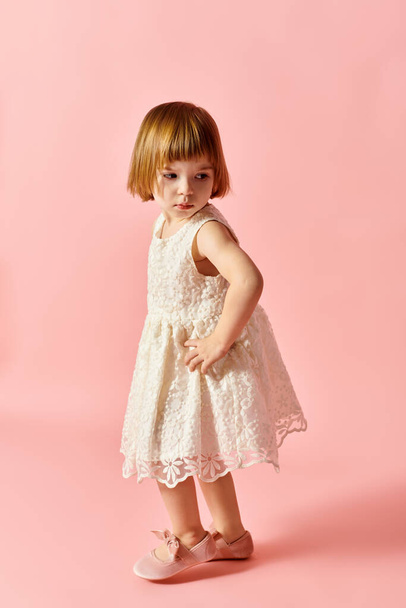 Little girl in white dress standing on pink backdrop. - Photo, Image
