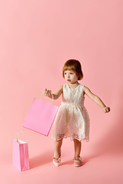 Little girl in white dress holding pink shopping bags on a pink background. - Photo, Image