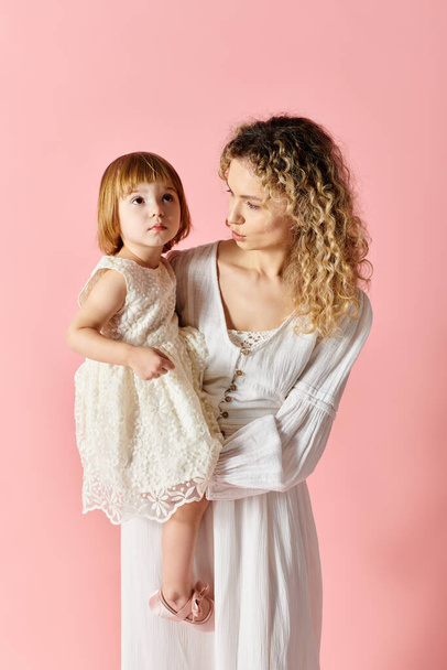 ピンクの背景に白いドレスで彼女の小さな女の子を抱いている母親. - 写真・画像