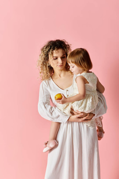 Γυναίκα κρατώντας το παιδί σε λευκό φόρεμα σε ροζ φόντο. - Φωτογραφία, εικόνα