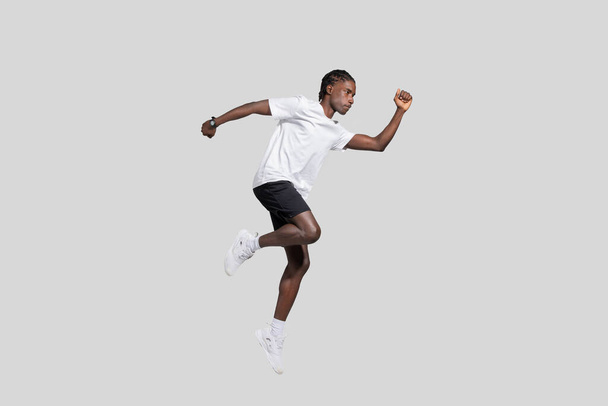 Joven chico afroamericano con construcción atlética capturado en el aire, ejemplificando la dinámica y la energía en un fondo llano - Foto, Imagen