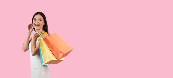A cheerful European lady carries multiple shopping bags, suggestive of a summer sale, appealing to Generation Z on an isolated pink background, copy space - Photo, Image