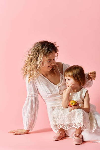 Adorable girl in white dress with curly-haired mom on vibrant pink backdrop. - Photo, Image
