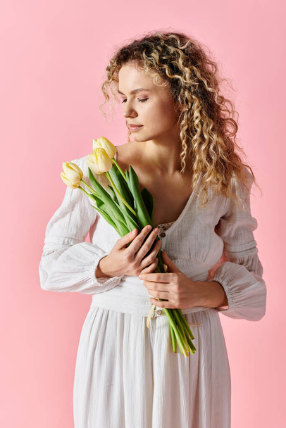 Stylish woman with curly hair holding colorful tulip bouquet on pink background. - Photo, Image