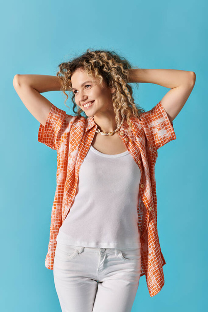 Femme aux cheveux bouclés en jean blanc et chemise orange frappant une pose. - Photo, image