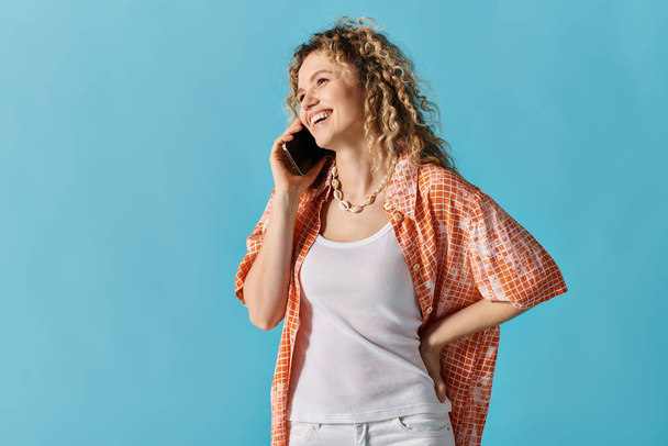 Woman with curly hair talking on cell phone against vibrant blue background. - Photo, Image