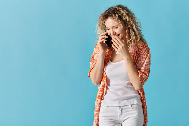 Γυναίκα με σγουρά μαλλιά κουβεντιάζοντας στο τηλέφωνο σε φωτεινό μπλε φόντο. - Φωτογραφία, εικόνα