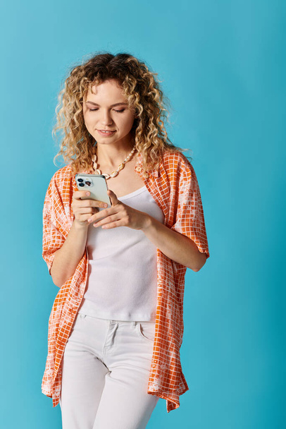 A fashionable woman with curly hair is absorbed in her phone. - Photo, Image