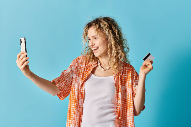 A woman with curly hair snaps a selfie holding a credit card. - Photo, Image