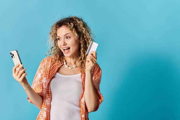 Woman with curly hair holding phone and credit card. - Photo, Image