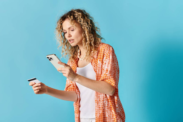 Mulher com cabelo encaracolado detém telefone celular e cartão de crédito. - Foto, Imagem