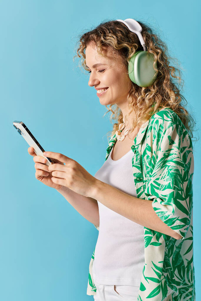Γυναίκα με σγουρά μαλλιά βυθισμένη στη μουσική μέσω ακουστικών και τηλεφώνου. - Φωτογραφία, εικόνα