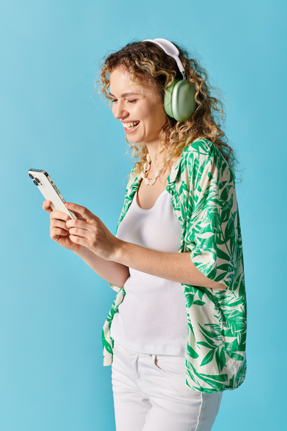 Кучерява жінка в навушниках, слухаючи музику на телефоні. - Фото, зображення