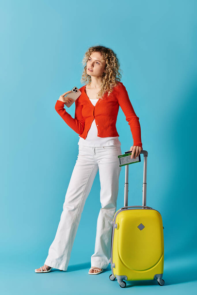 Una mujer con una maleta amarilla posa sobre un vibrante fondo azul. - Foto, imagen