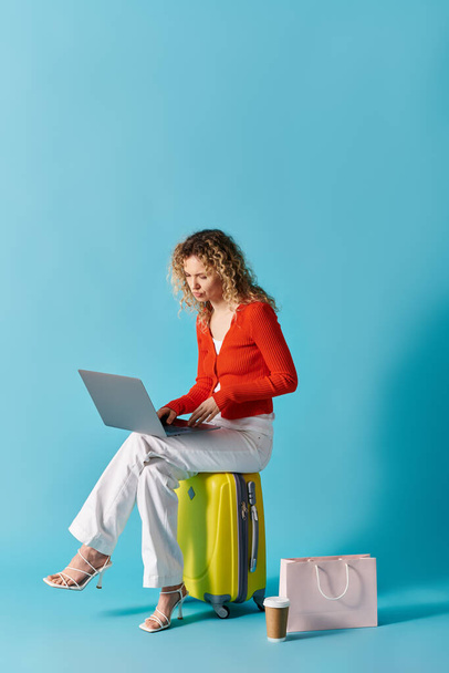 Woman sitting on a suitcase, using a laptop. - Photo, Image