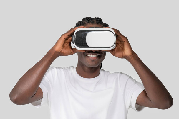 Afrikai-amerikai fiatal srác elmerült egy virtuális élmény, kezében egy VR headset egy egyszerű háttér, kiemelve a modern szórakoztató technológia - Fotó, kép