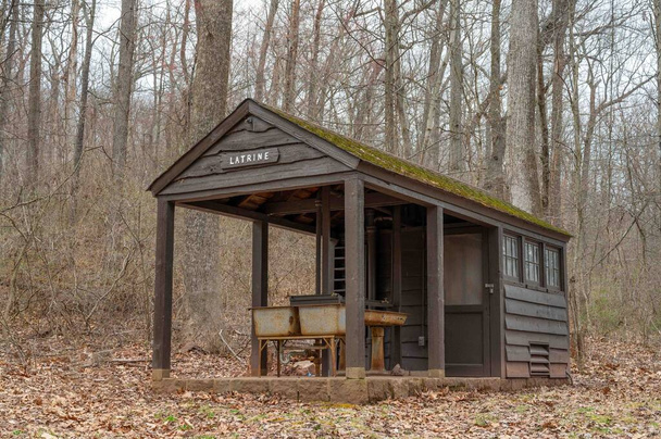 Bruine houten hut stijl latrine met oude roestige wastafels en een bord omgeven door hoge bomen in een bosrijke natuur achtergrond geen mensen met kopieerruimte. - Foto, afbeelding
