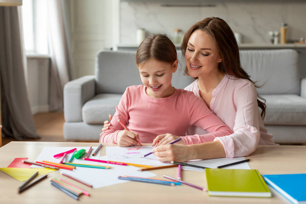 Мать помогает дочери с домашним заданием, делясь близким и радостным моментом обучения в уютном интерьере дома, копировать пространство - Фото, изображение
