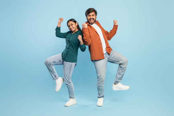 Energetic and happy Indian couple celebrating, posing with fists raised in a victory stance on blue - Photo, Image