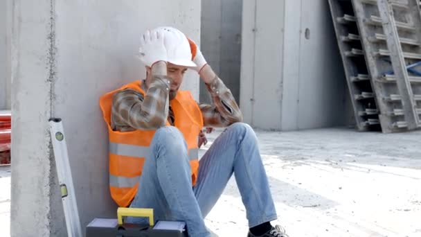 Costruttore riparatore, caposquadra in casco di sicurezza e giubbotto seduto a riposare sul posto di lavoro nell'edificio accanto alla cassetta degli attrezzi e al righello - Filmati, video