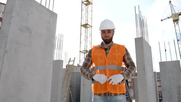 Builder repairman, foreman in protective helmet and vest stands at workplace in building and holds ruler in hands - Footage, Video