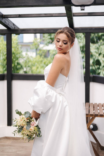 Gyönyörű menyasszony gyönyörű esküvői ruha áll a teraszon, és várja a vőlegény. Kiváló minőségű fénykép - Fotó, kép