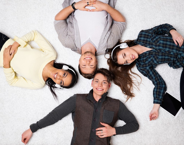 Happy multiracial friends relaxing on a carpet with gadgets  - Photo, Image