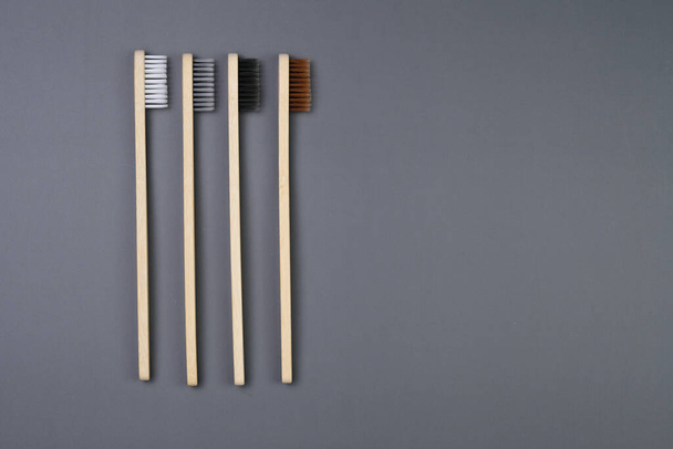 Três escovas de dentes de bambu eco-friendly são dispostas ordenadamente em um fundo cinza sólido. As escovas de dentes não são marcadas e mostram o grão natural do material de bambu.. - Foto, Imagem