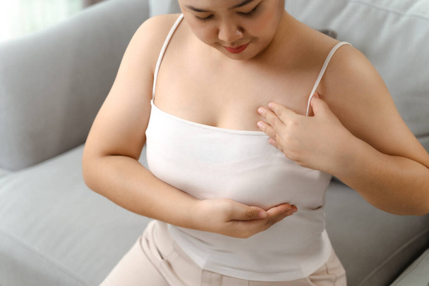 Femme asiatique vérifiant des grumeaux sur son sein pour des signes de cancer du sein par elle-même à la maison. Soins de santé et concept médical. - Photo, image